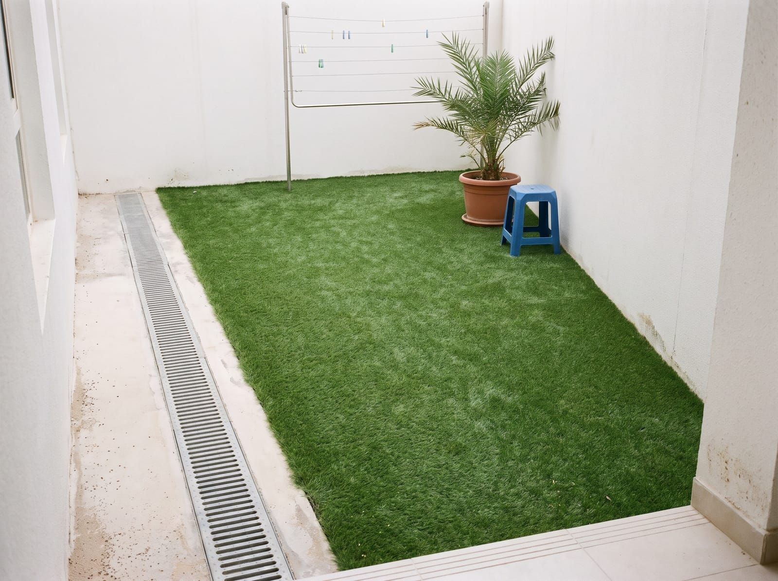 A small concrete courtyard covered in artificial grass, with a steel drainage channel left clear along one side