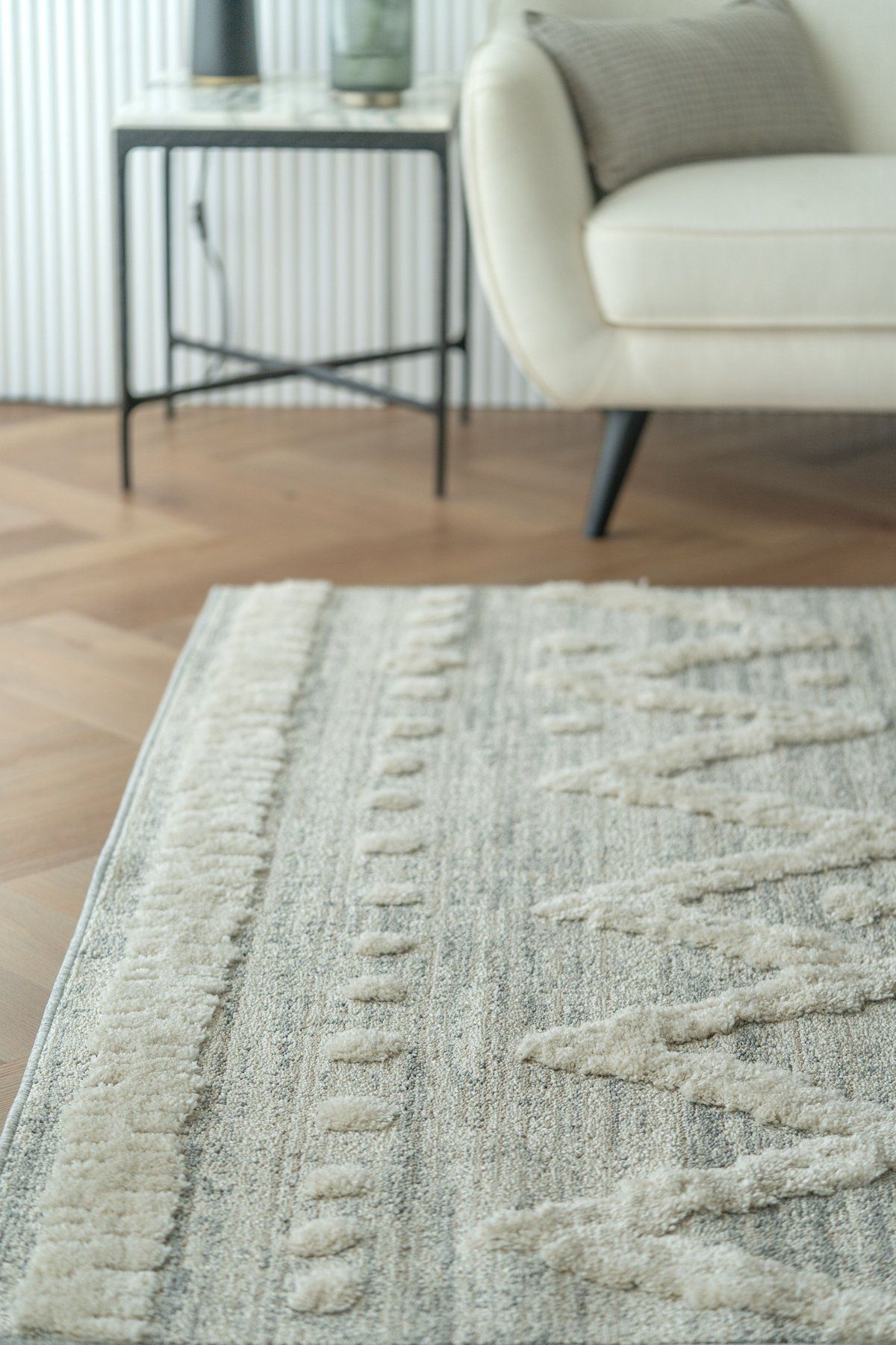 An ivory textured rug on a herringbone wooden floor, the legs of a chair and table at its edge