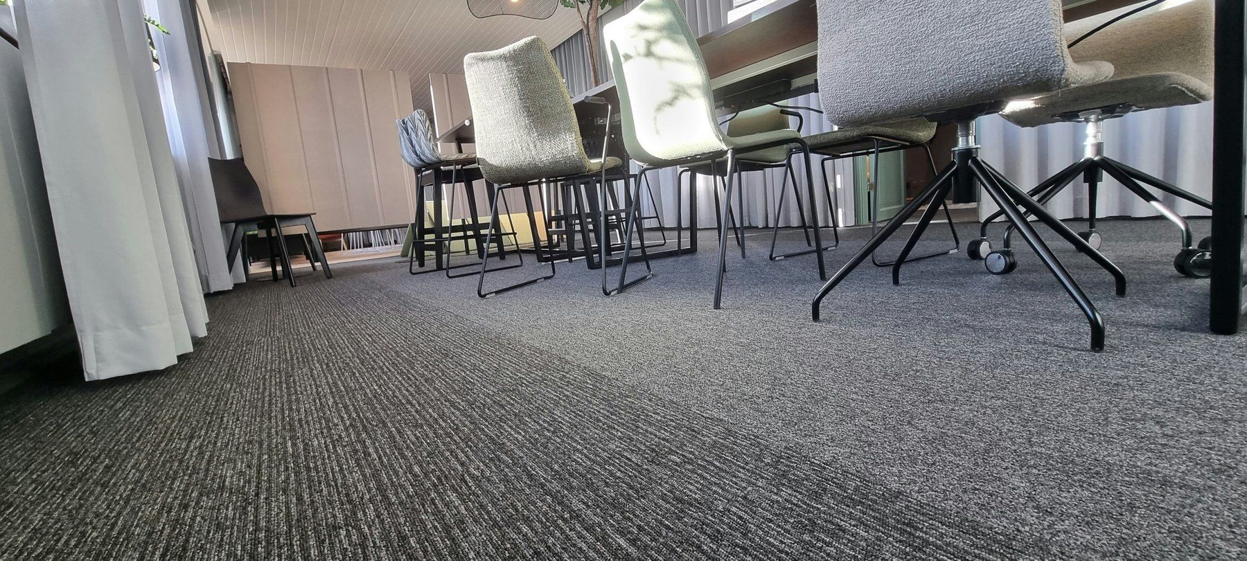 Grey carpet tiles across an office floor, seen at floor level under desk chairs