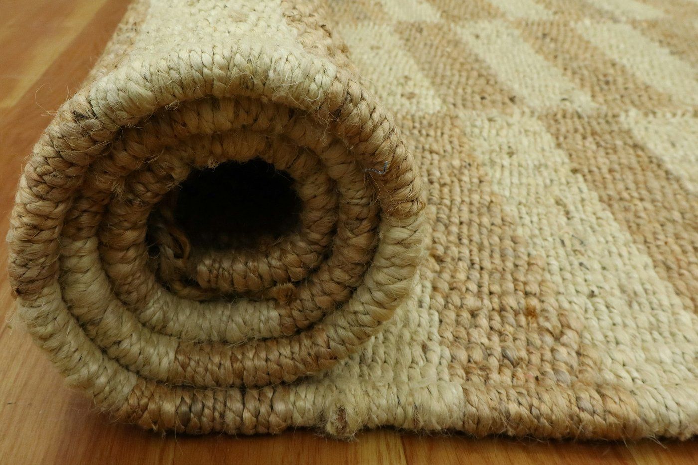 A jute rug rolled up on a wooden floor, ready to be laid
